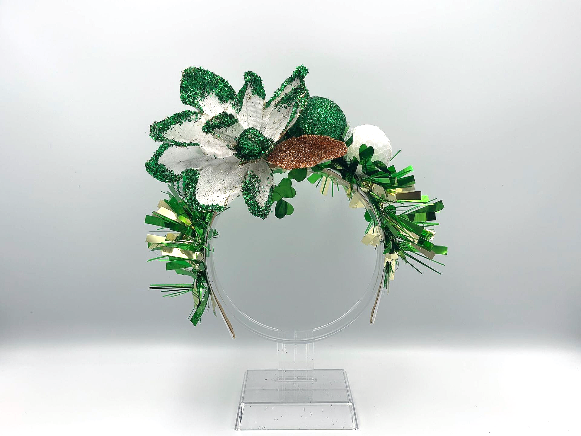 Green and white floral headband on a clear stand, with sparkly accents.