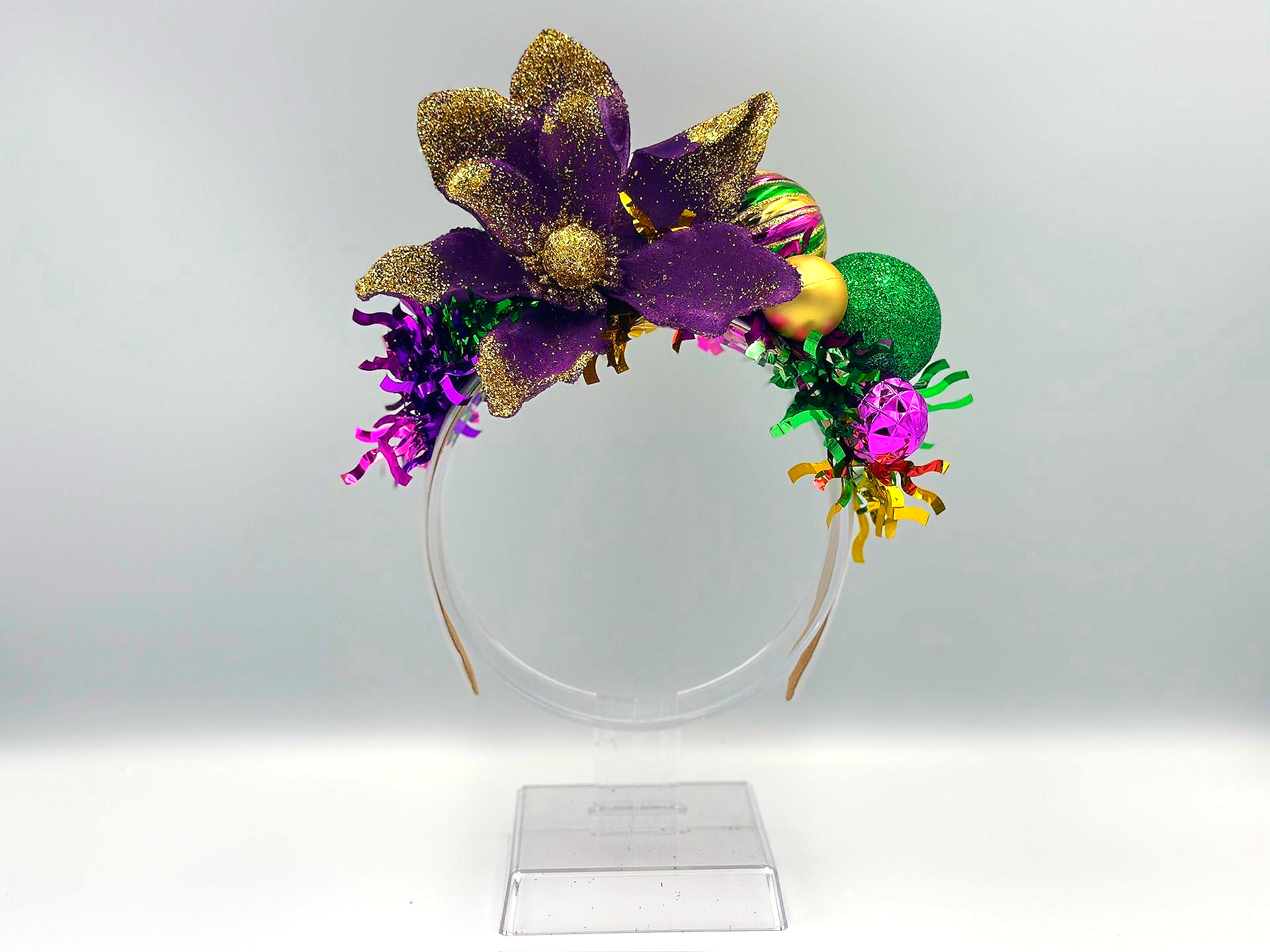 Mardi Gras headband with purple, gold, and green decorations, including flowers and ornaments on a clear band.