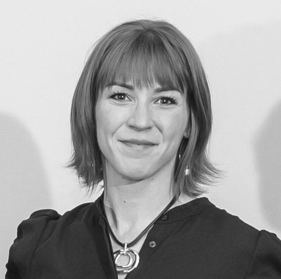 A woman with light hair and a black shirt smiling without teeth