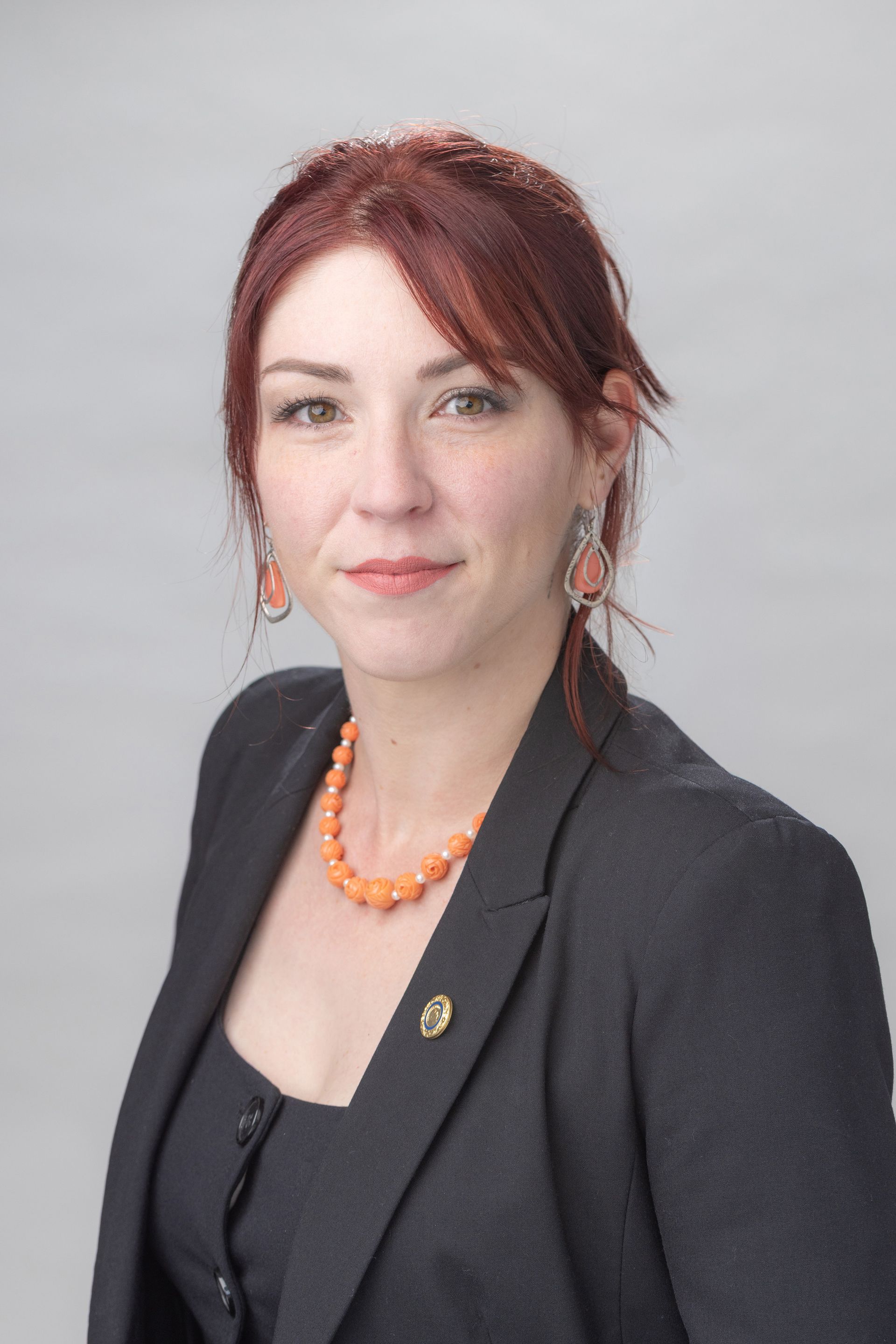 A woman with red hair is smiling while wearing a black shirt with a silver necklace