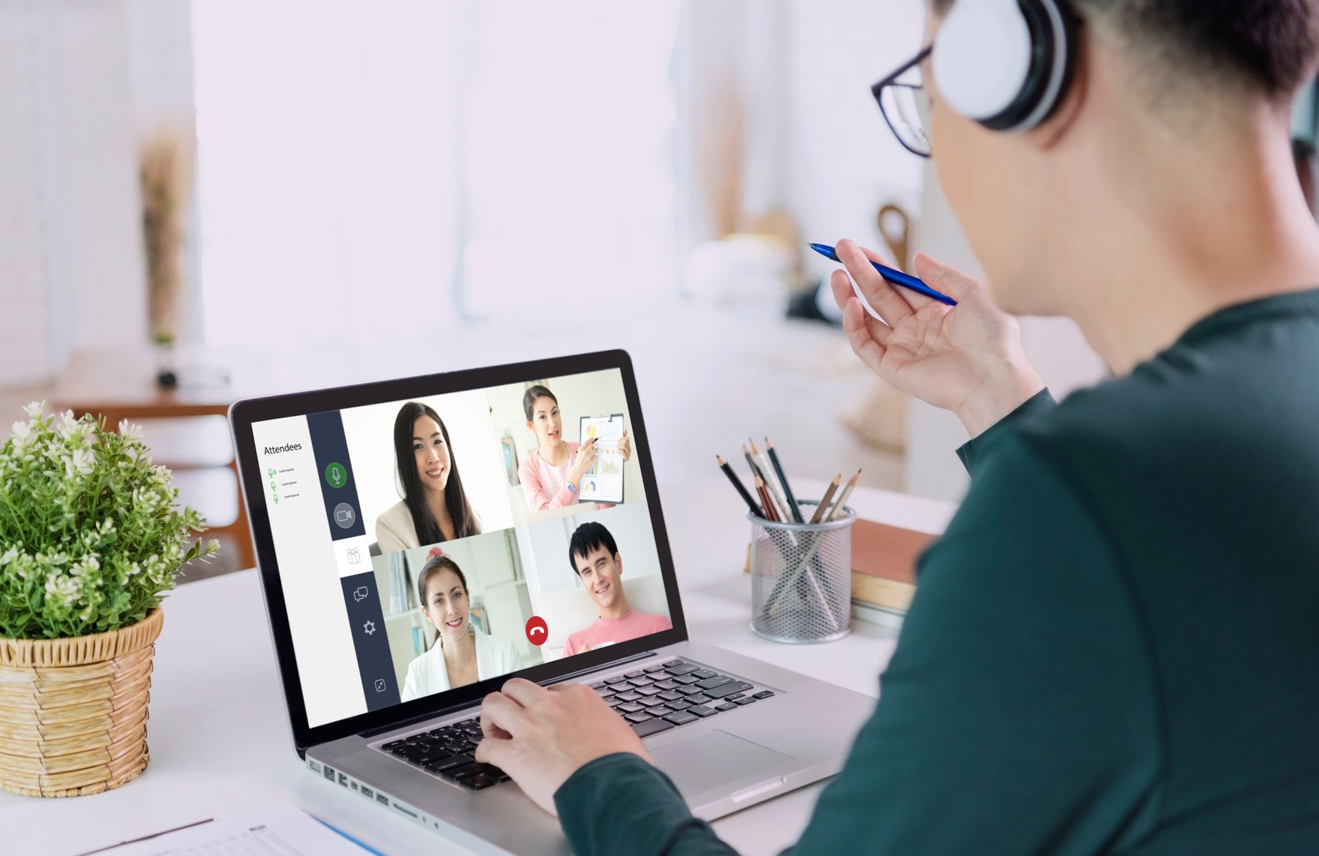 Man in headphones on a video call, laptop on a desk; four others on the screen.