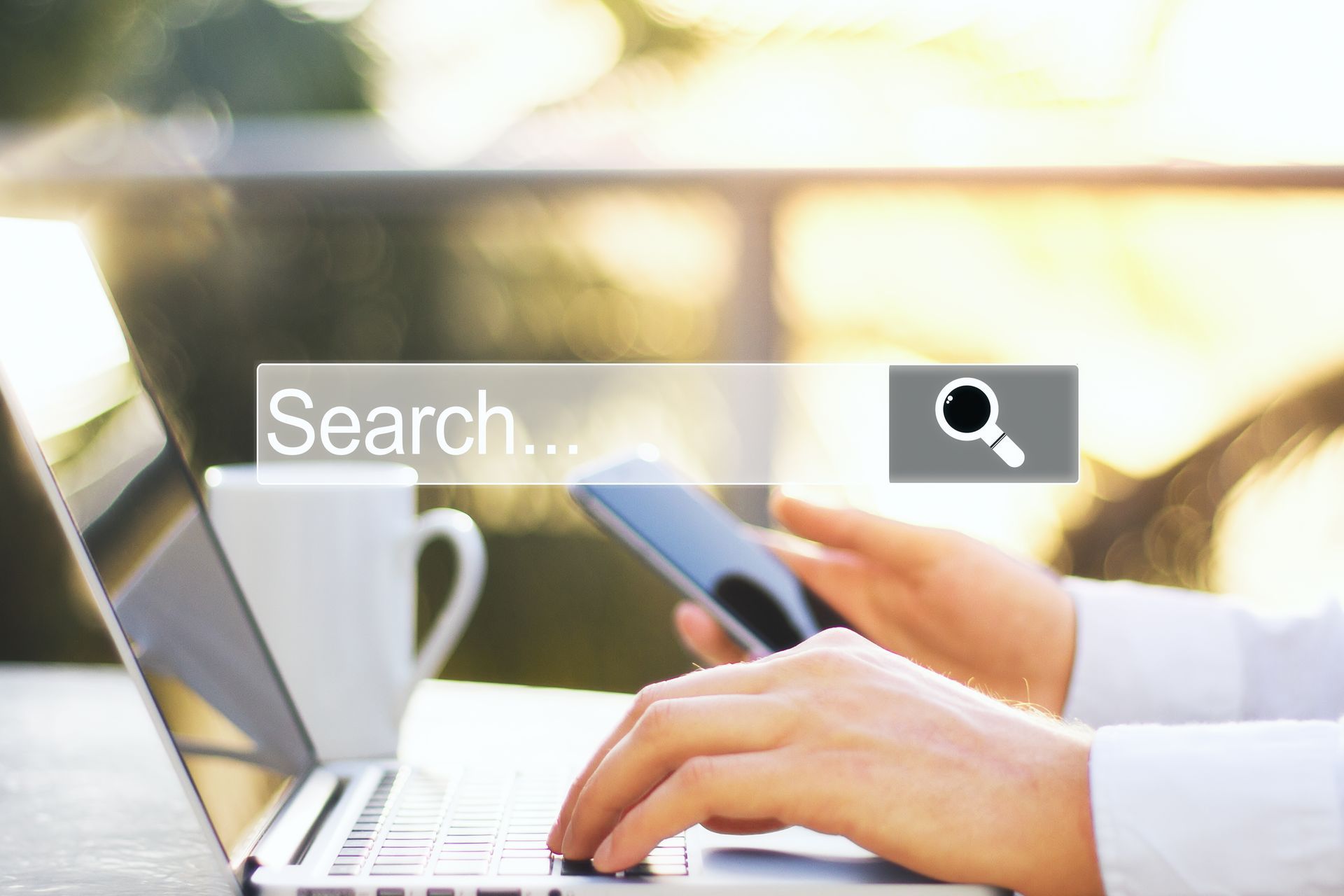 Person using a laptop and phone, typing, with search bar overlay. Outdoor setting.