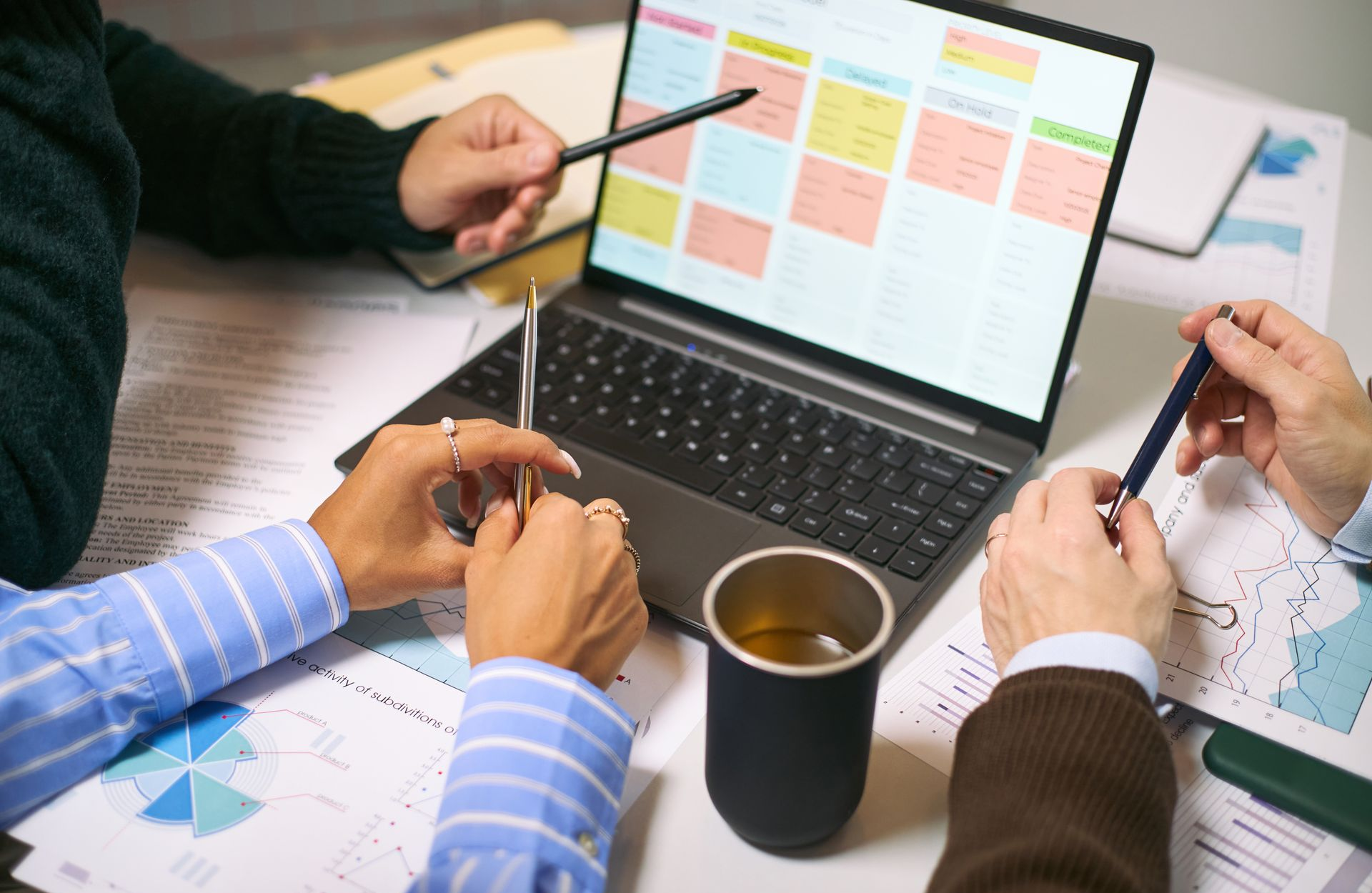 People around a laptop with a calendar, pointing at the screen, papers scattered, discussing plans.