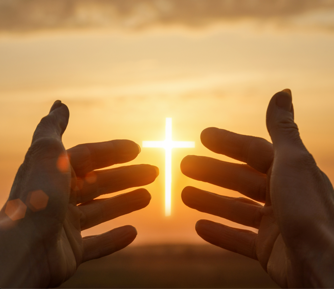 A person is holding a cross in their hands at sunset
