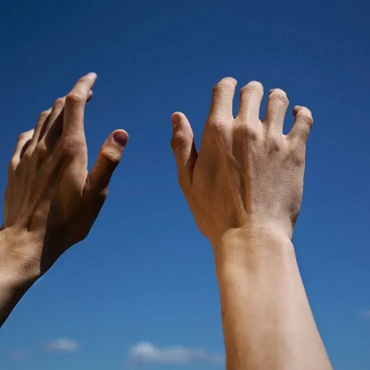 Two hands are reaching up into the blue sky