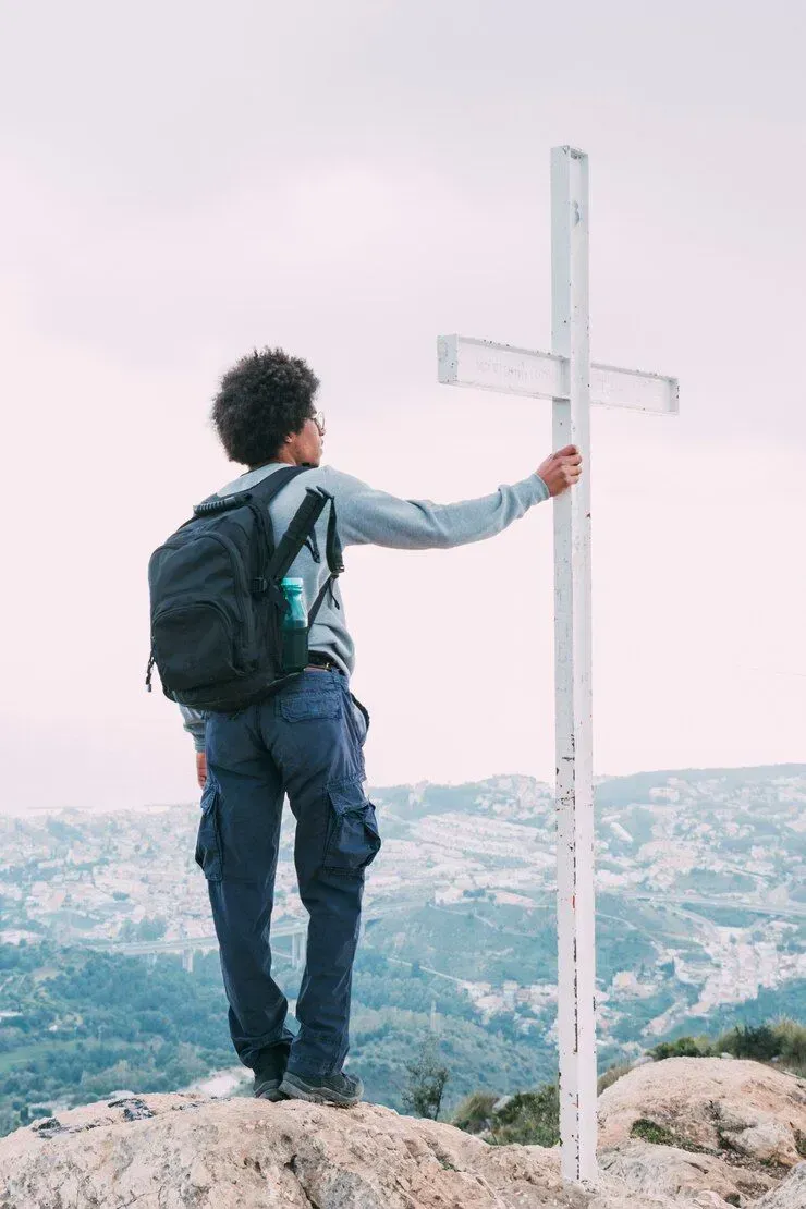 A man with a backpack is standing on top of a mountain holding a cross.