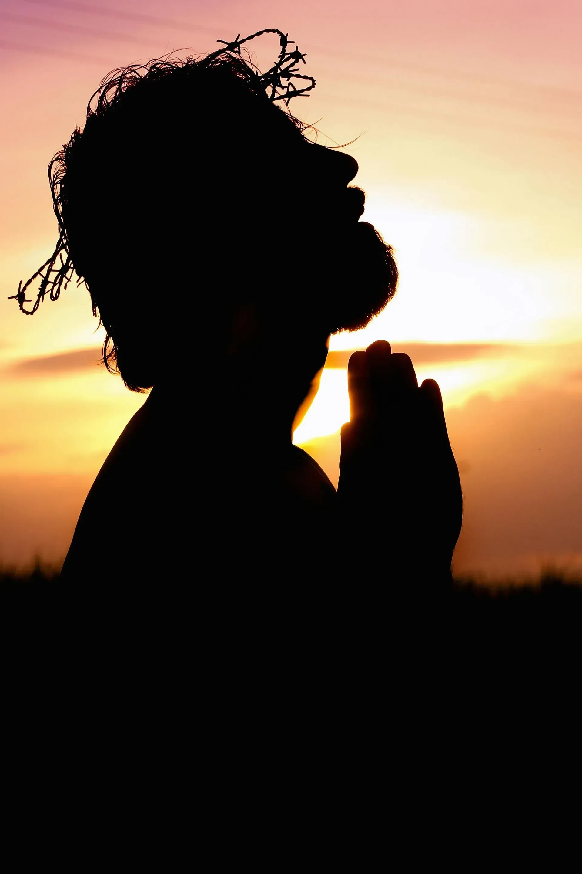 A silhouette of a man praying at sunset