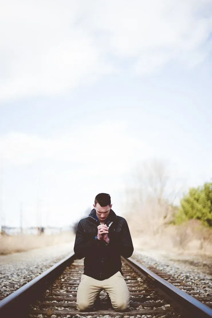 A man is kneeling on train tracks and praying.