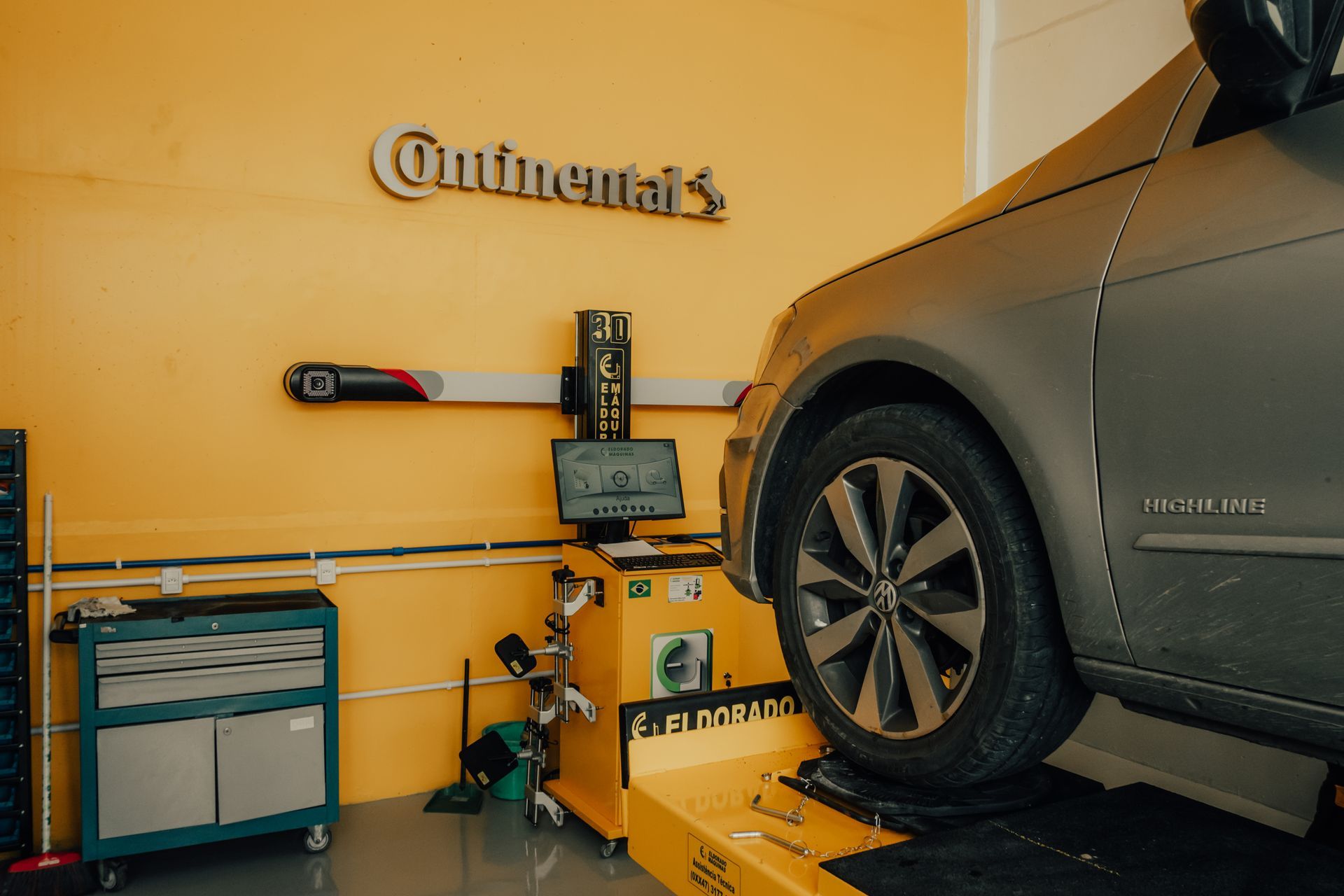 Mecânico inspecionando um pneu de carro em uma oficina, usando luvas e uniforme azul.