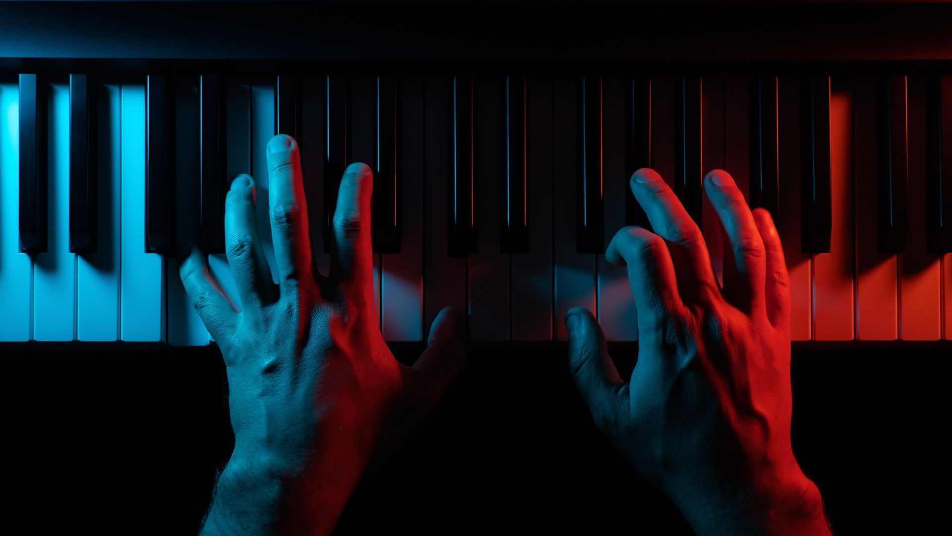 A person is playing a piano in a dark room with red and blue lights.