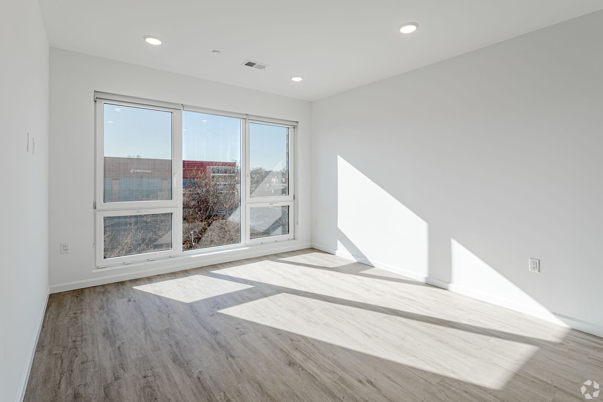 An empty living room with hardwood floors and large windows.- The Unity