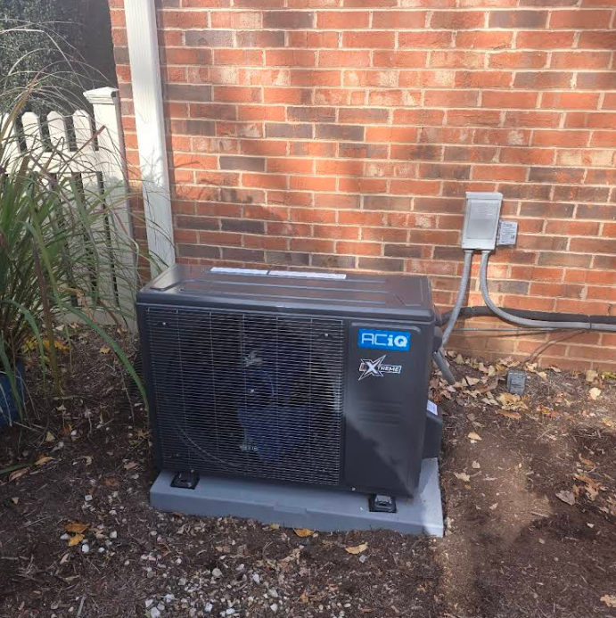 Black Riello outdoor HVAC unit beside a brick wall and electrical conduit.