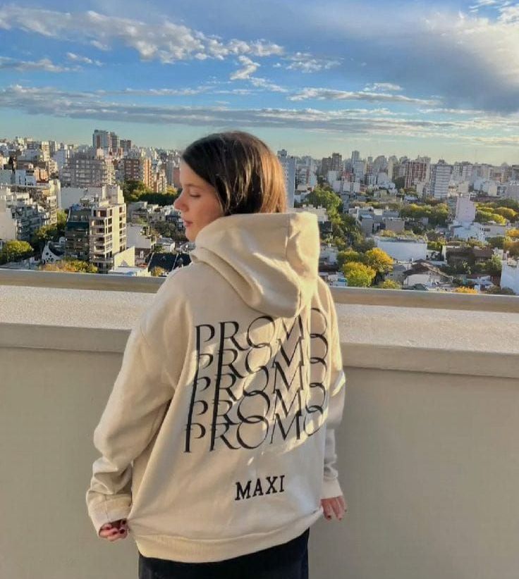 Una mujer con una sudadera con capucha está parada en un balcón con vistas a una ciudad.