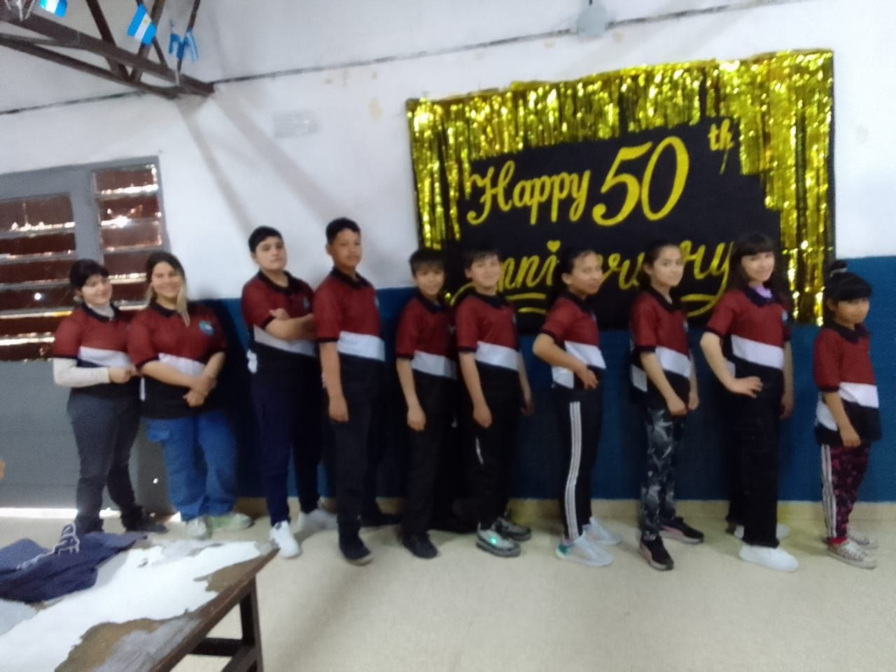 Un grupo de niños de pie frente a un cartel que dice feliz 50 aniversario.