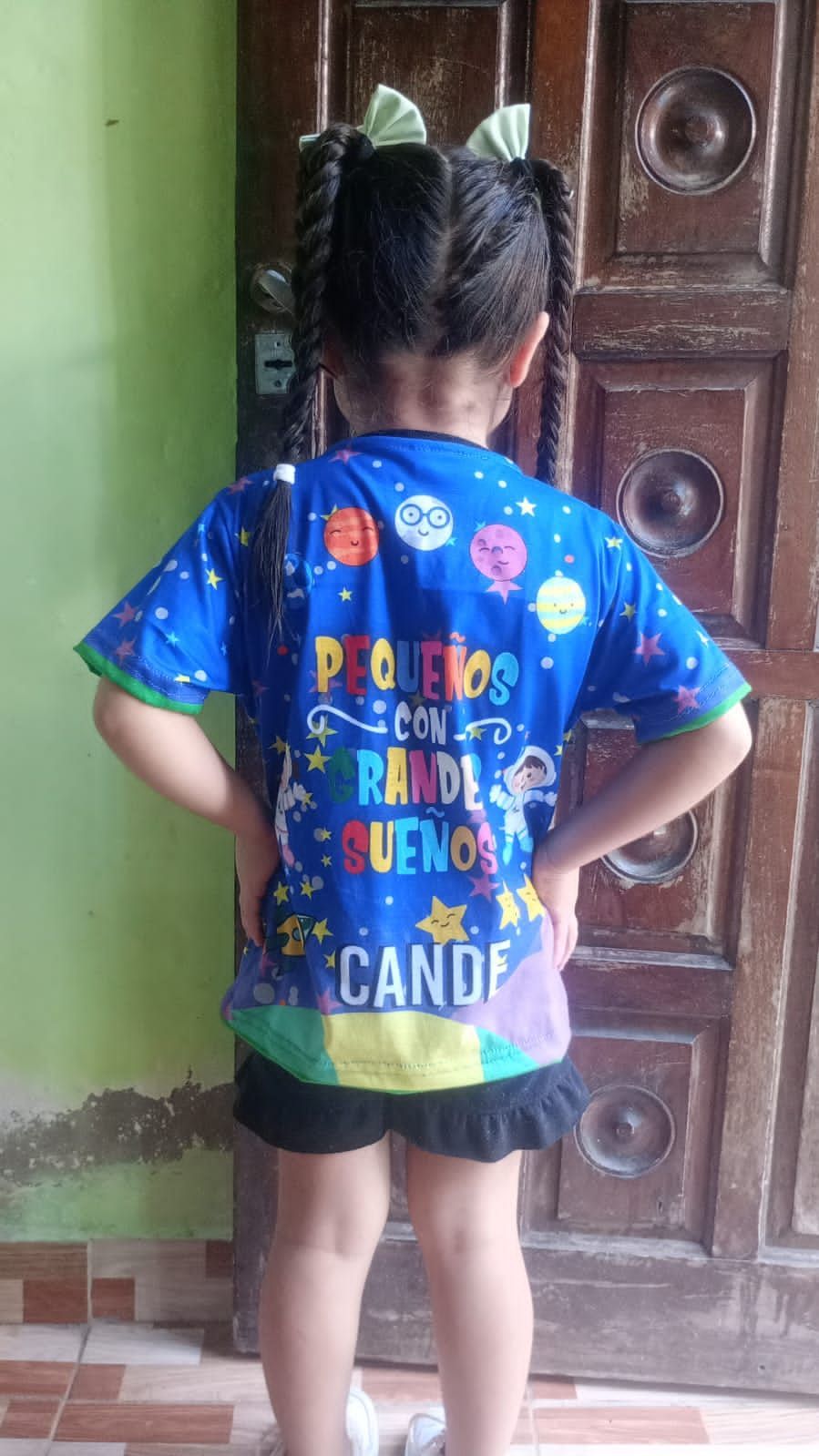 Una niña está parada frente a una puerta vistiendo una camisa azul.