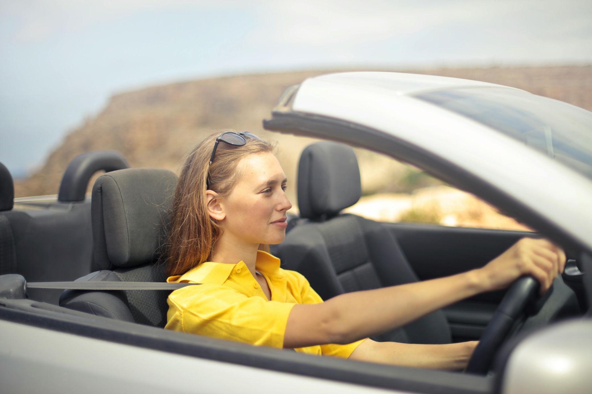 A woman in a yellow shirt is driving a convertible car.