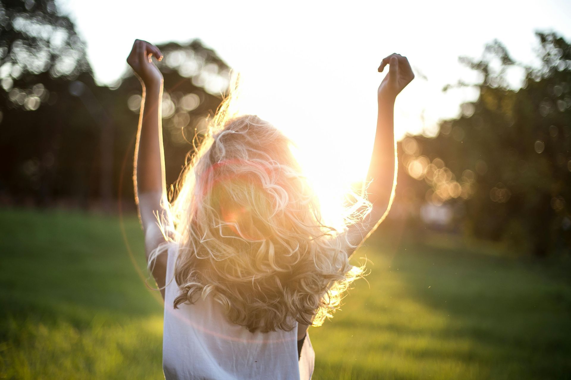 A woman is standing in a field with her arms in the air.