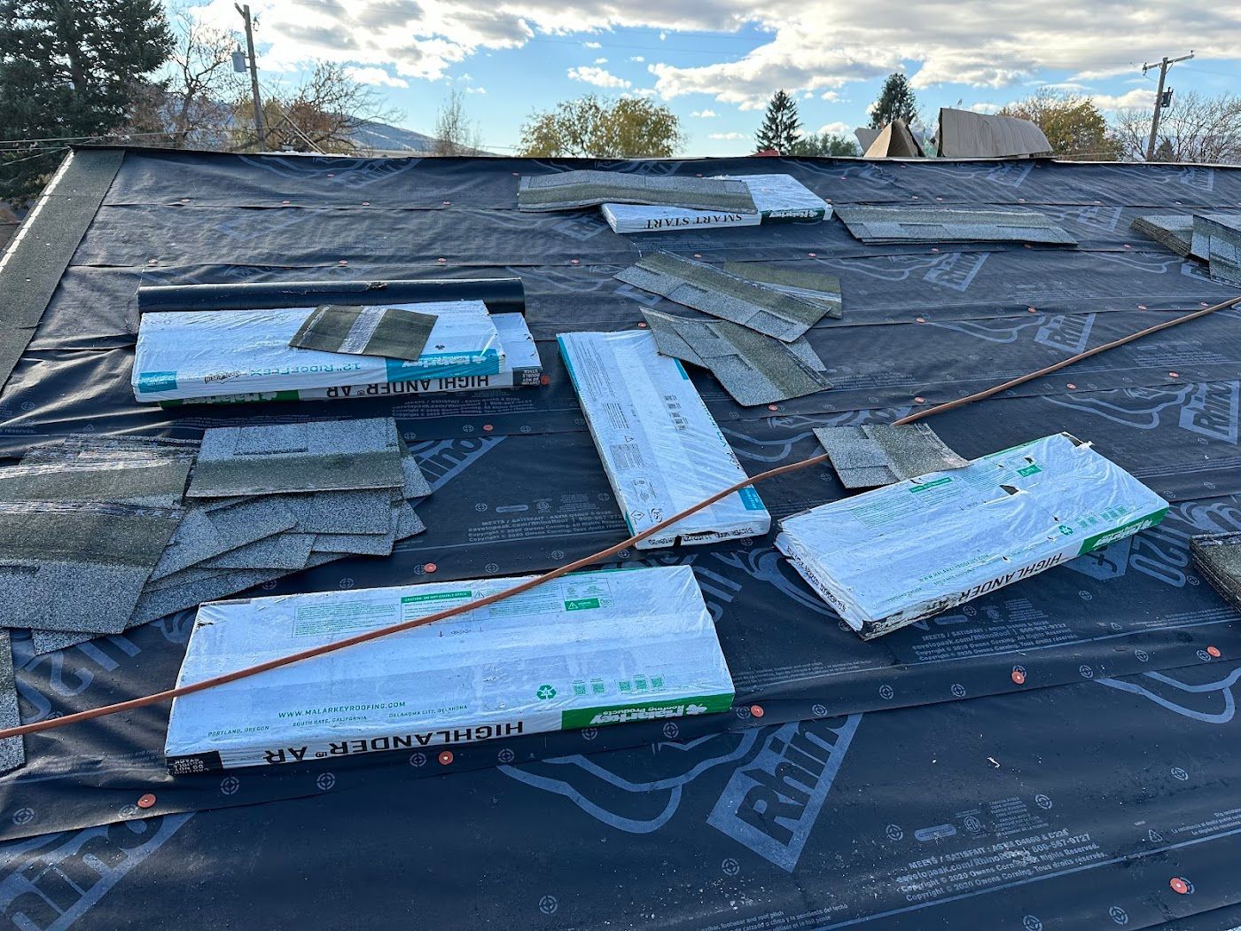 A roof undergoing repairs, featuring stacks of shingles and underlayment laid out on the black protective paper.
