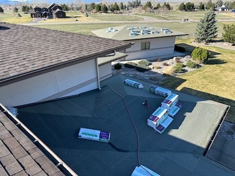 High-angle view of a flat roof under repair, featuring stacked roofing material bundles and a surrounding landscape.