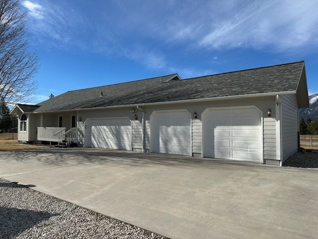 Light-colored single-story house with a three-car garage and a front porch under a clear blue sky.