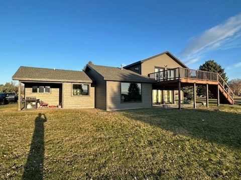 A taupe two-story house with a backyard deck and covered patio stands under a clear blue sky on a sunny day.