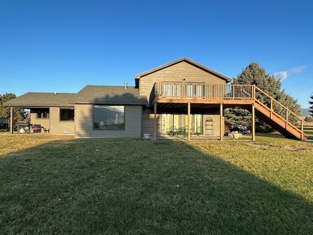 A two-story tan home features a large wooden deck with stairs extending down to a grassy backyard under a clear blue sky.