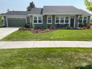 A one-story gray house with a two-car garage, white trim, and a manicured lawn under a clear blue sky.