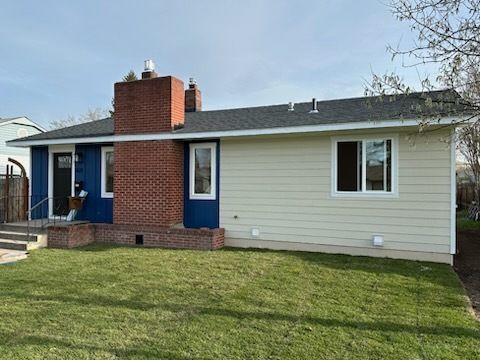 A single-story house with a brick chimney, blue accents around the front entrance, and light yellow horizontal siding.