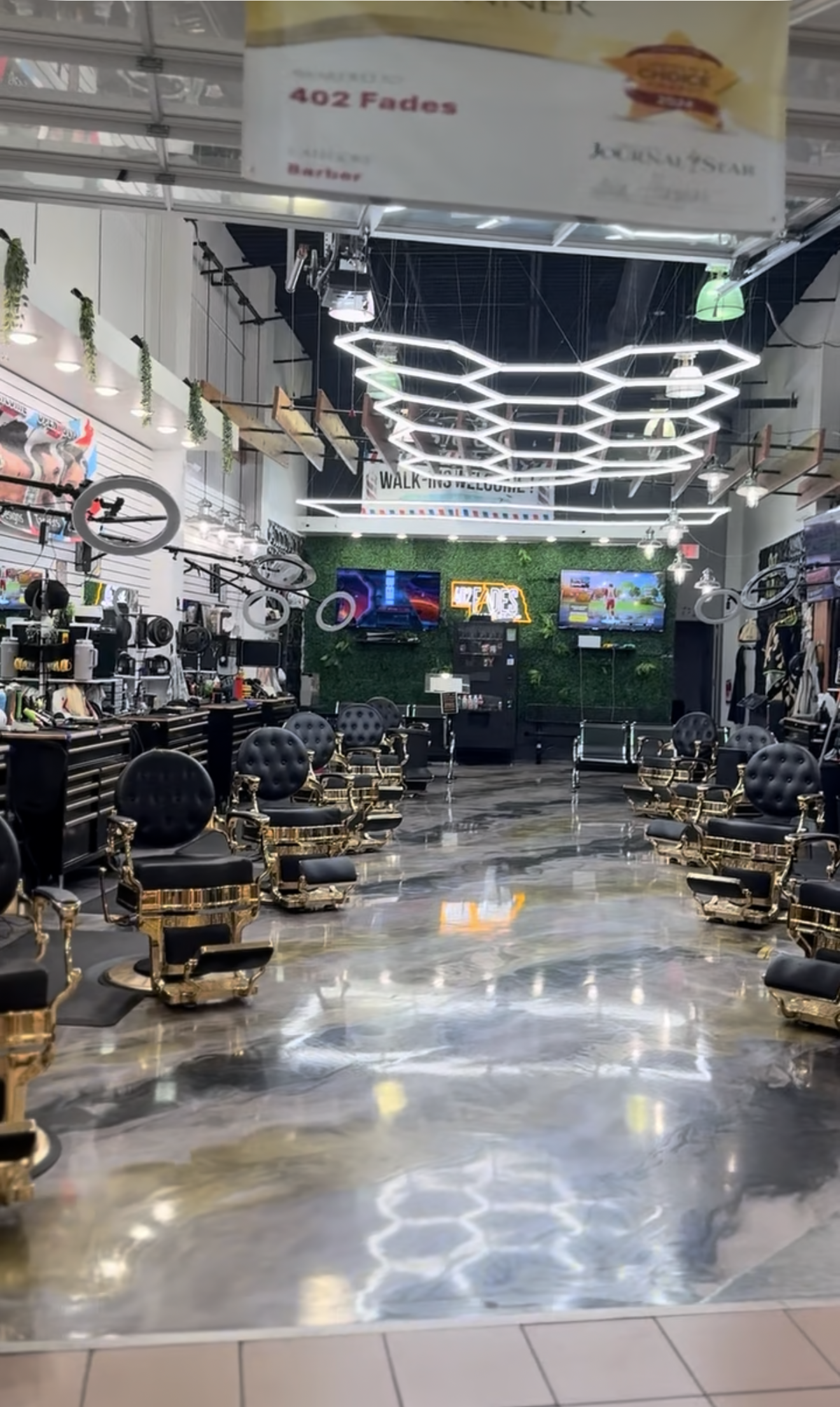 Modern barbershop interior featuring rows of black leather styling chairs, metallic epoxy floors, and hexagonal lighting.