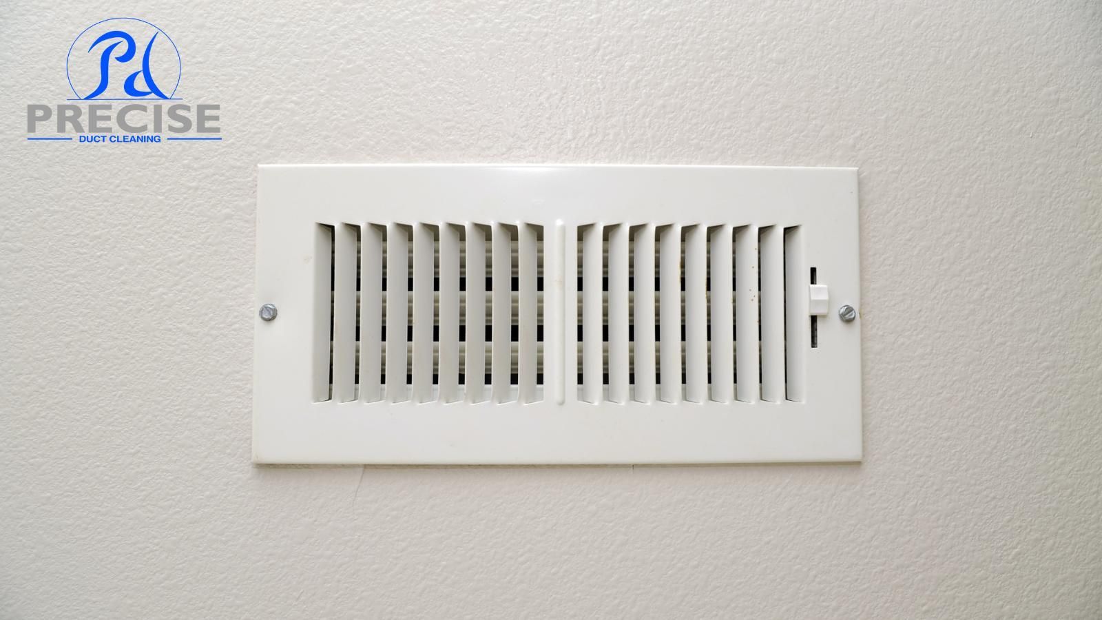 A white air vent is hanging on a white wall.With Precise Duc Cleaning's logo in the left corner