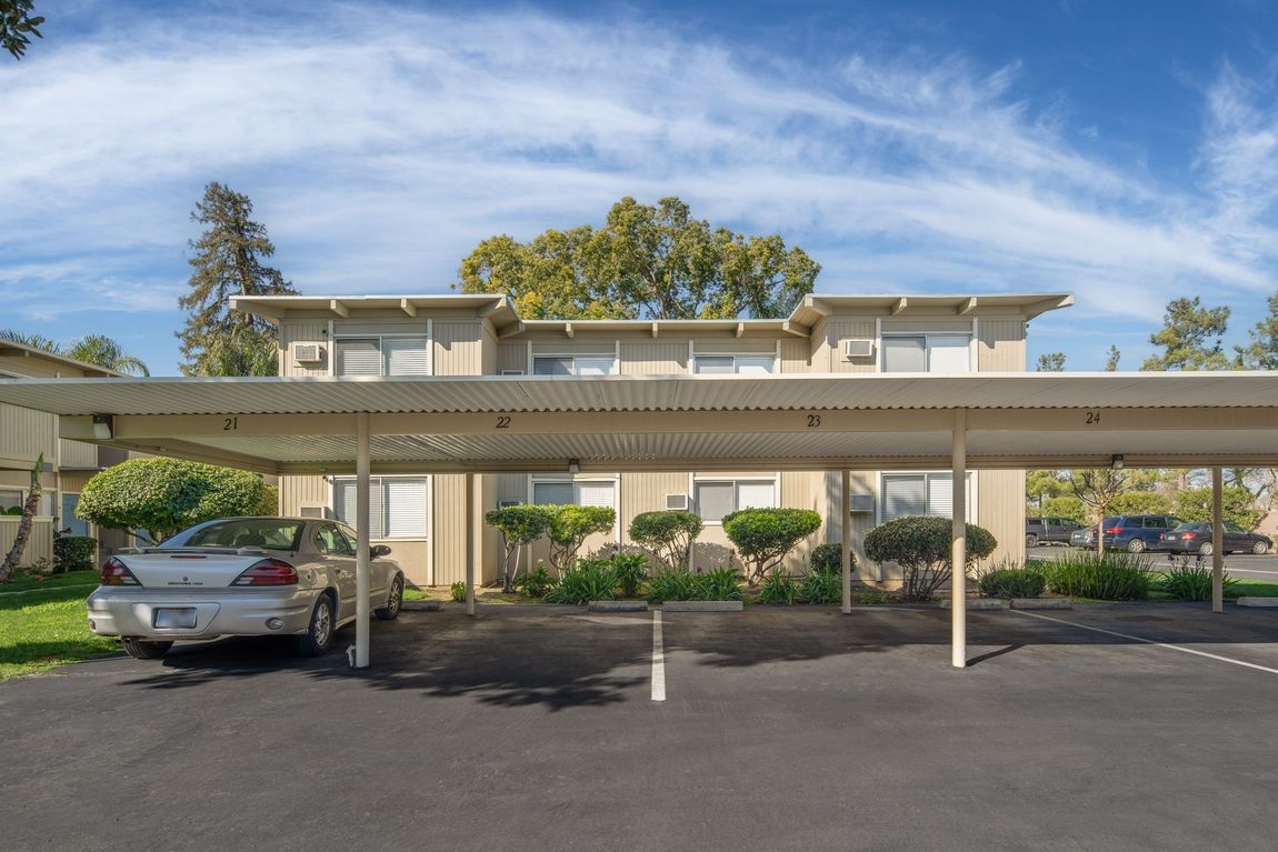 A beige apartment building with a covered parking area; a car is parked beneath the cover.