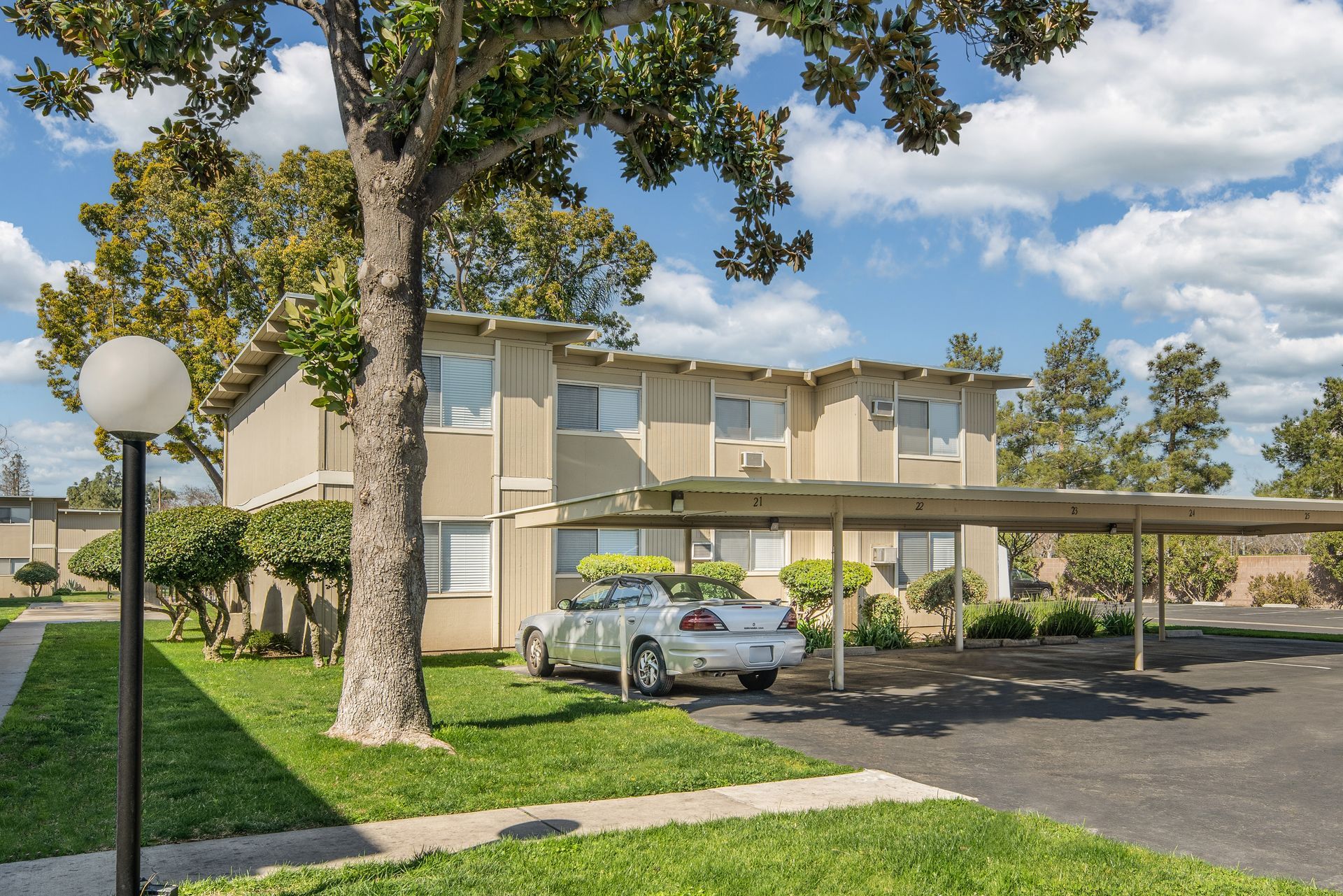 Two-story apartment building with covered parking and a car, under a blue sky.