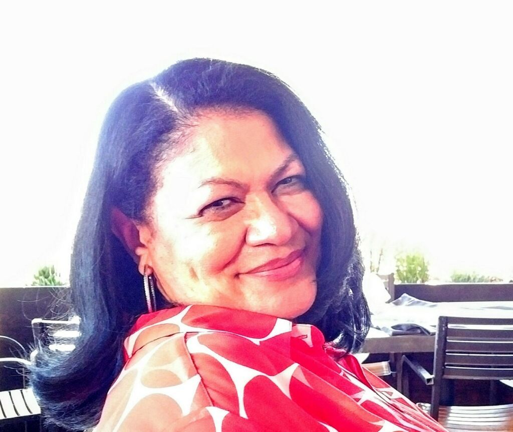 Smiling woman with blue-tinted hair, wearing a red and white patterned top, outdoors.