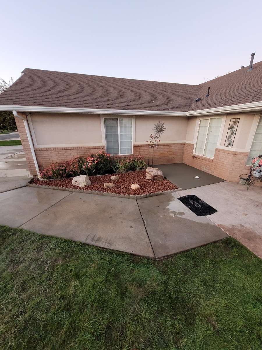 A view of a tan home exterior with a concrete walkway leading to the front door, featuring a landscaped garden area.