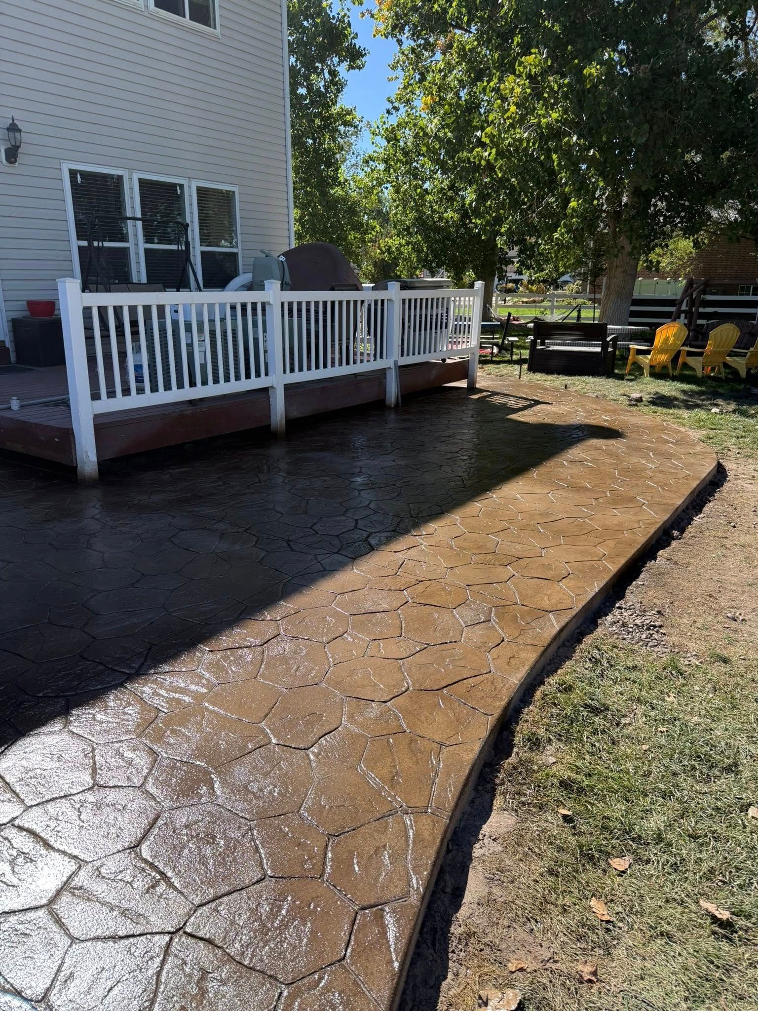 Stamped concrete patio with a dark, cracked-stone pattern next to a residential deck with white railings.