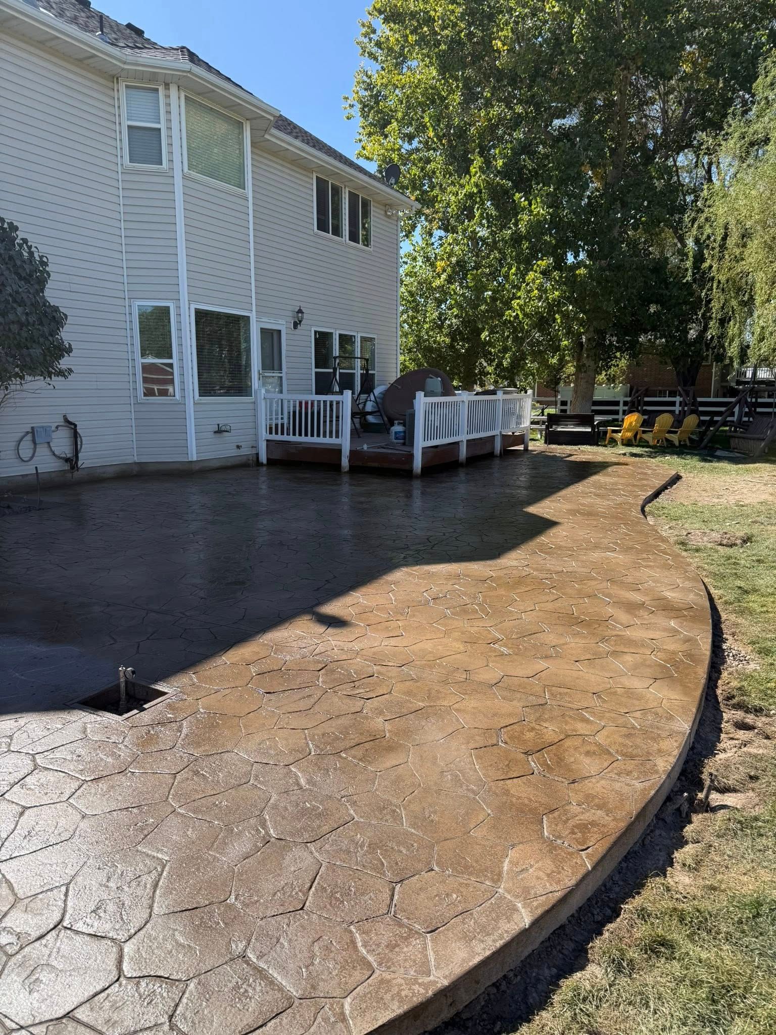 A stamped concrete patio in a backyard extends from a house with white siding and a small white deck.