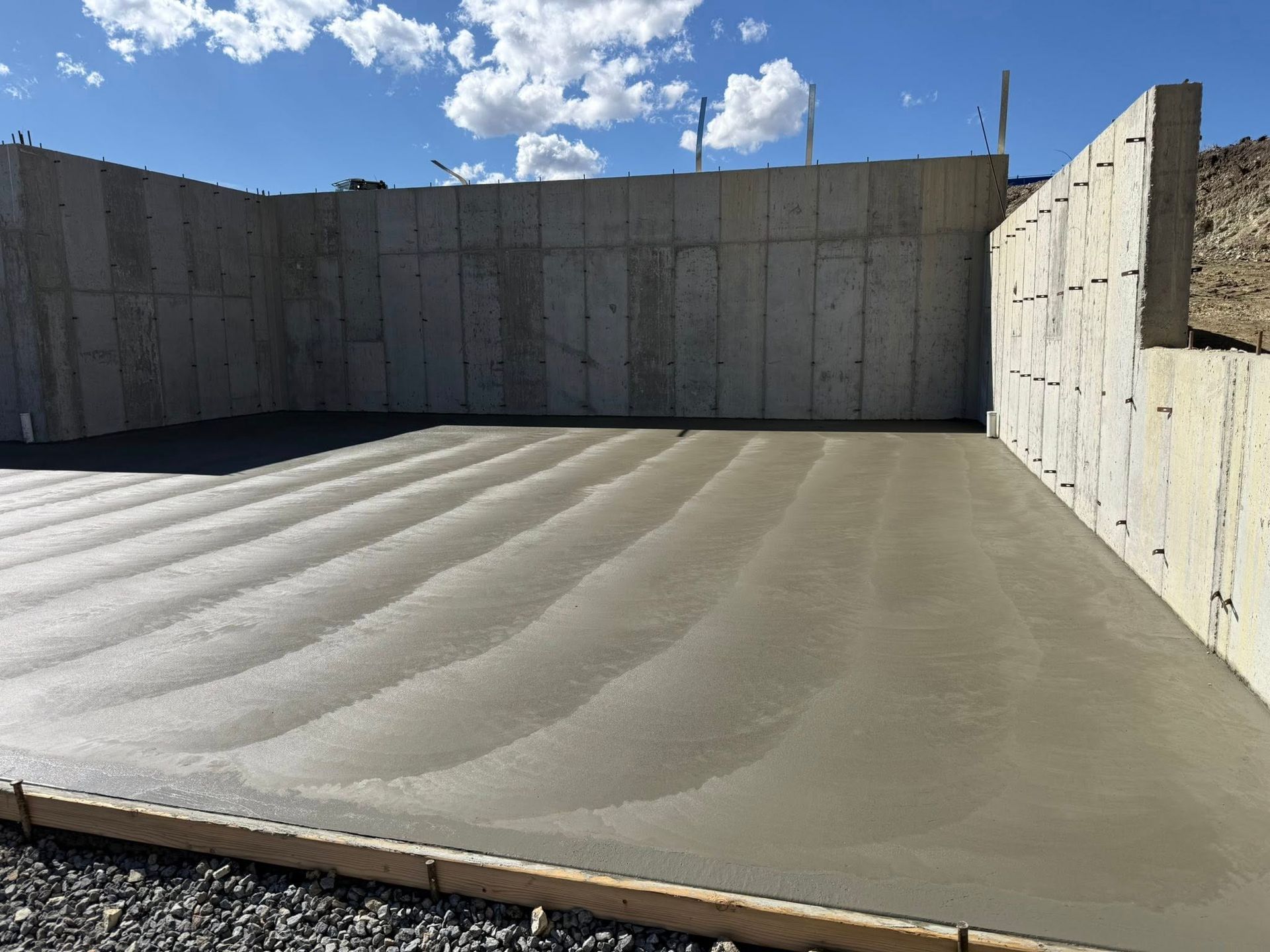 Newly poured, wet concrete floor inside a foundation wall structure on a bright, sunny day.
