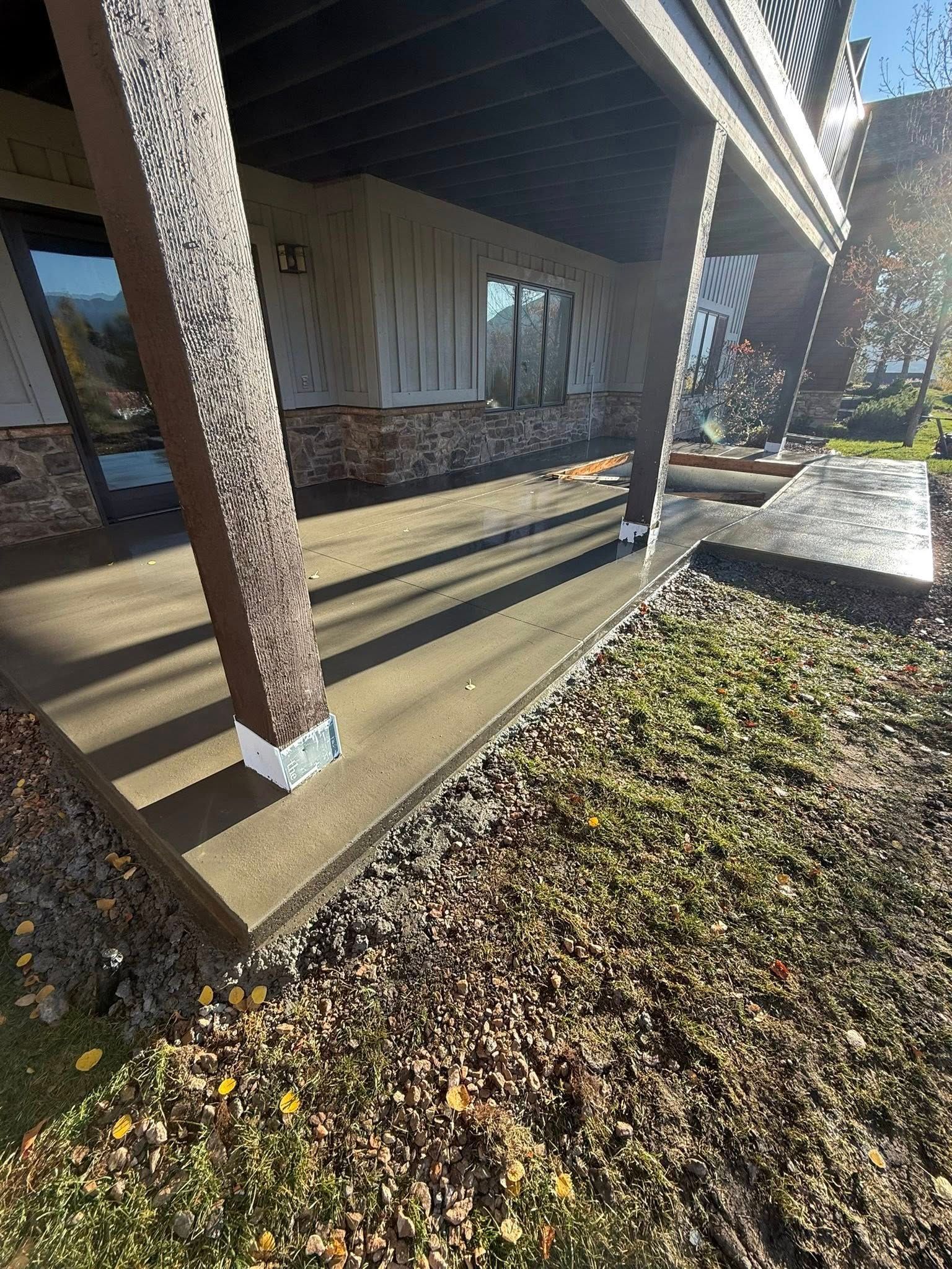 A ground-level view of a house patio with dark support columns and a stone-accented exterior wall overlooking a gravel lawn.