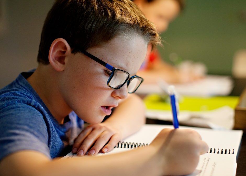 A young boy wearing glasses is writing in a notebook.