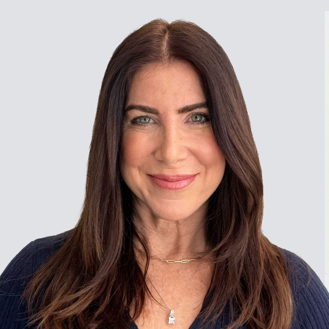 A woman wearing a denim vest is smiling for the camera.