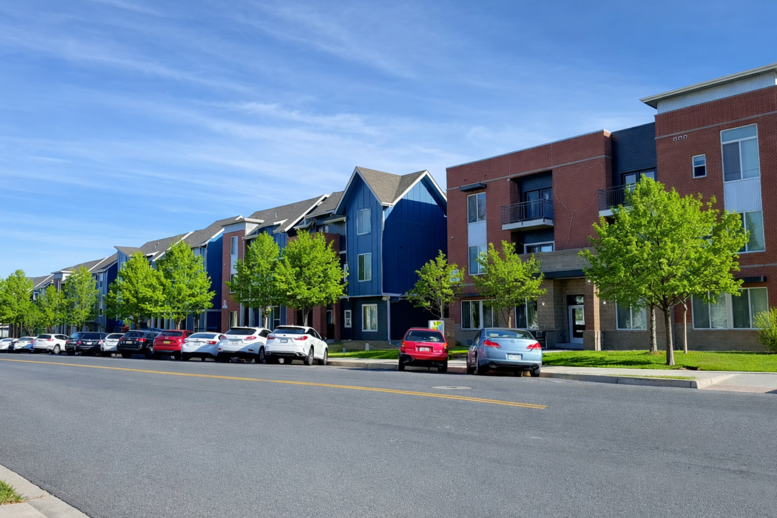 Colorful townhouses and parked cars along a sunny residential street under a clear blue sky