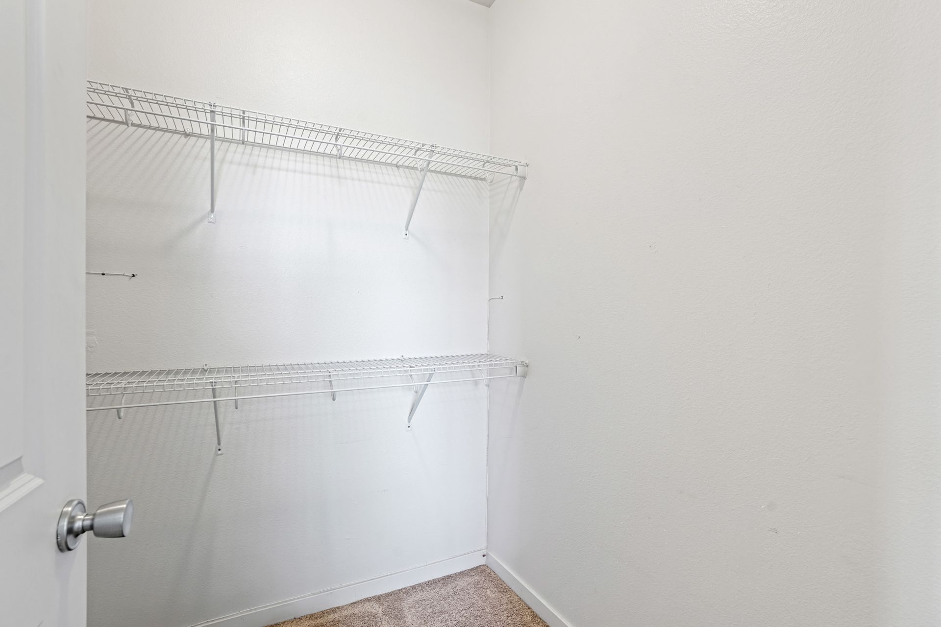 Empty white laundry room with wire shelving and a door handle on the left.