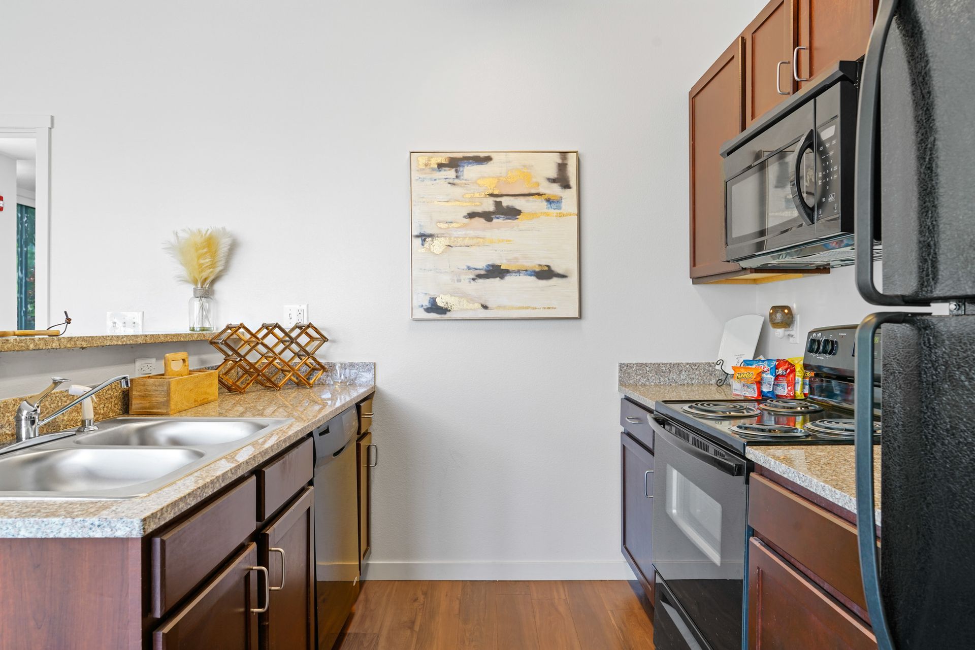 Modern kitchen with dark cabinets, granite counters, stainless appliances, and wall art