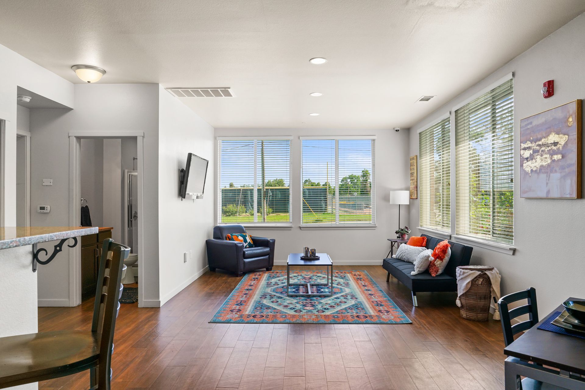 Bright living room with two dark sofas, blue rug, coffee table, and large windows overlooking green hills.