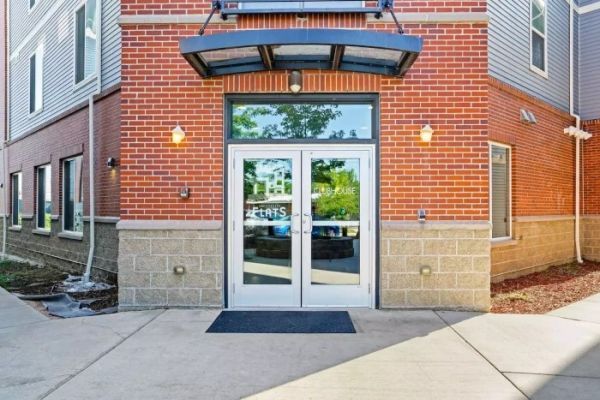 Brick apartment building entrance with glass double doors, awning, and concrete walkway