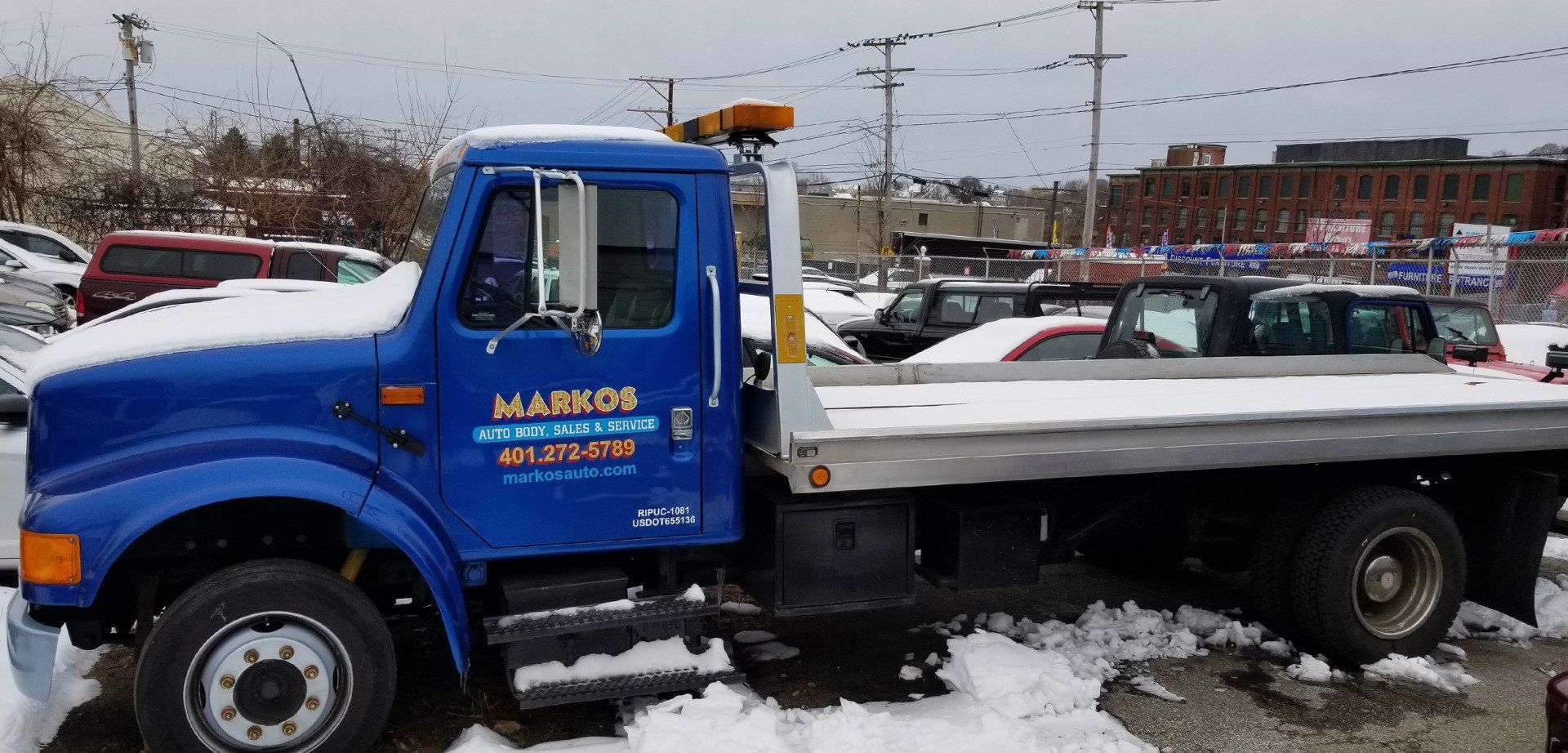 A blue tow truck is parked in the snow in a parking lot.