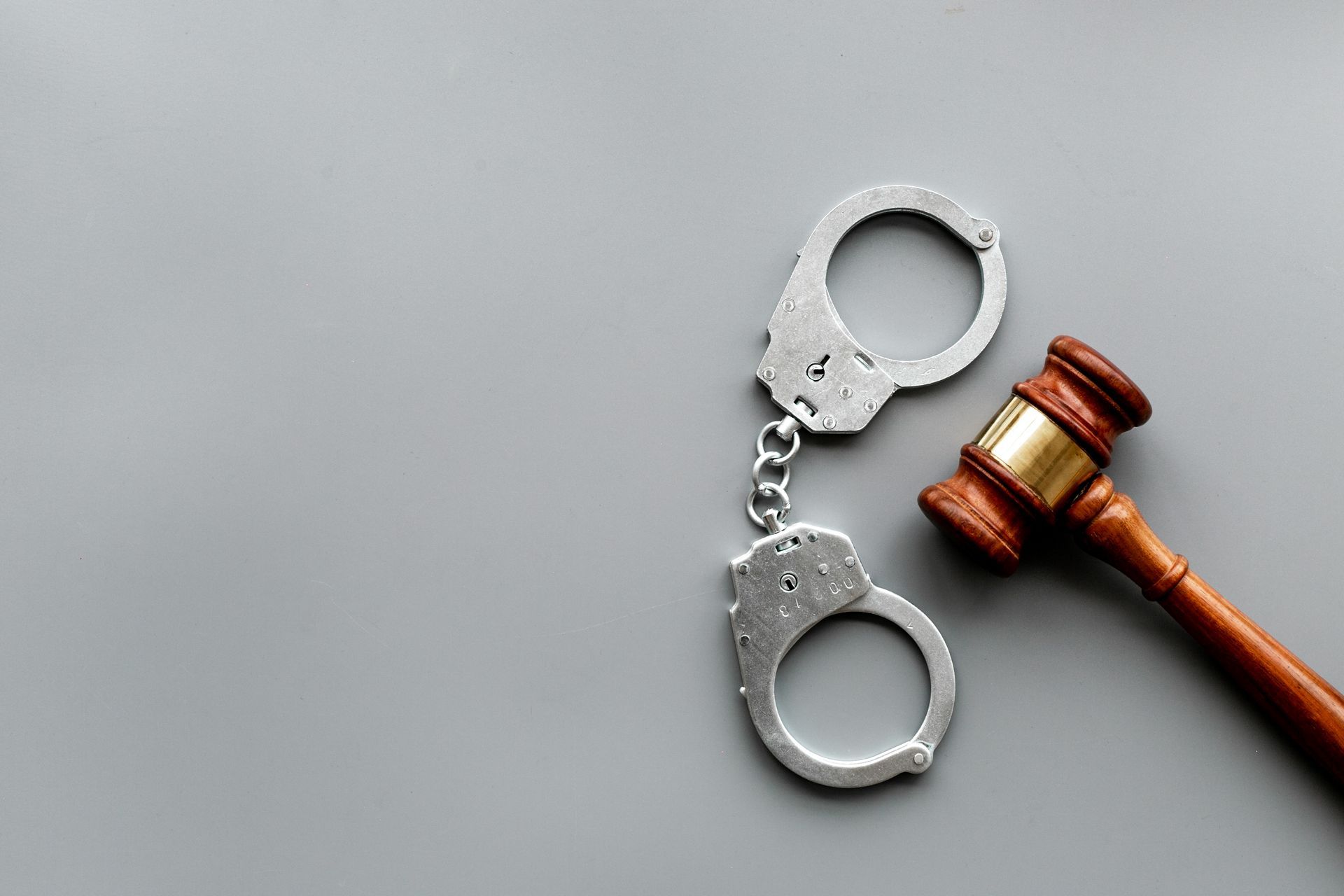 A pair of handcuffs and a judge 's gavel on a gray background.