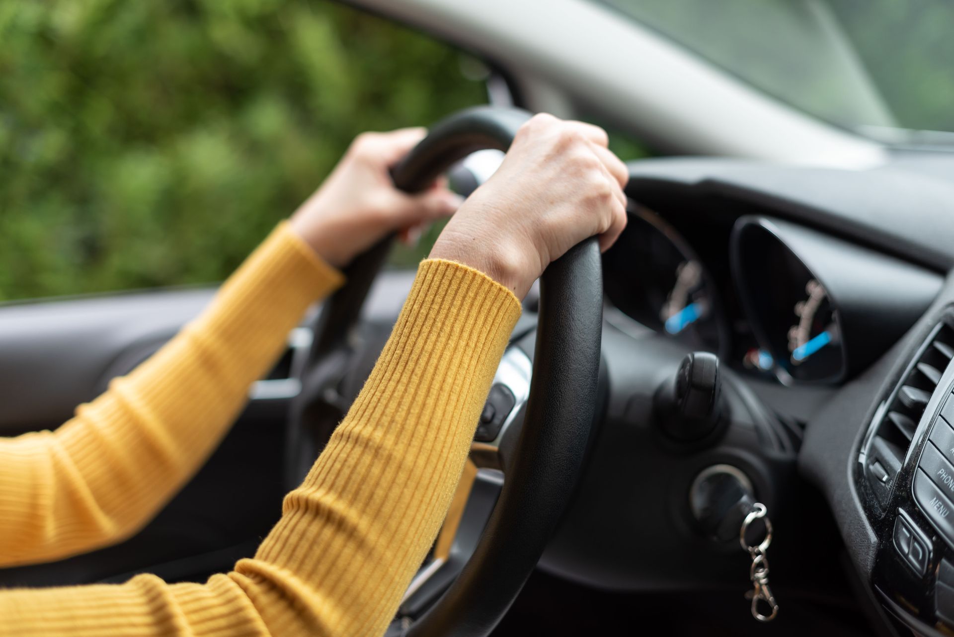 A woman in a yellow sweater is driving a car.
