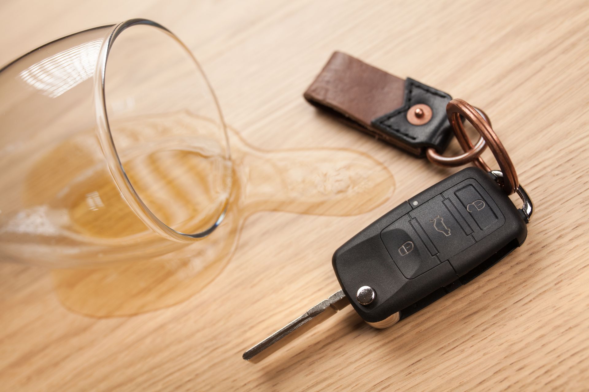 A car key next to a spilled glass of wine on a wooden table.