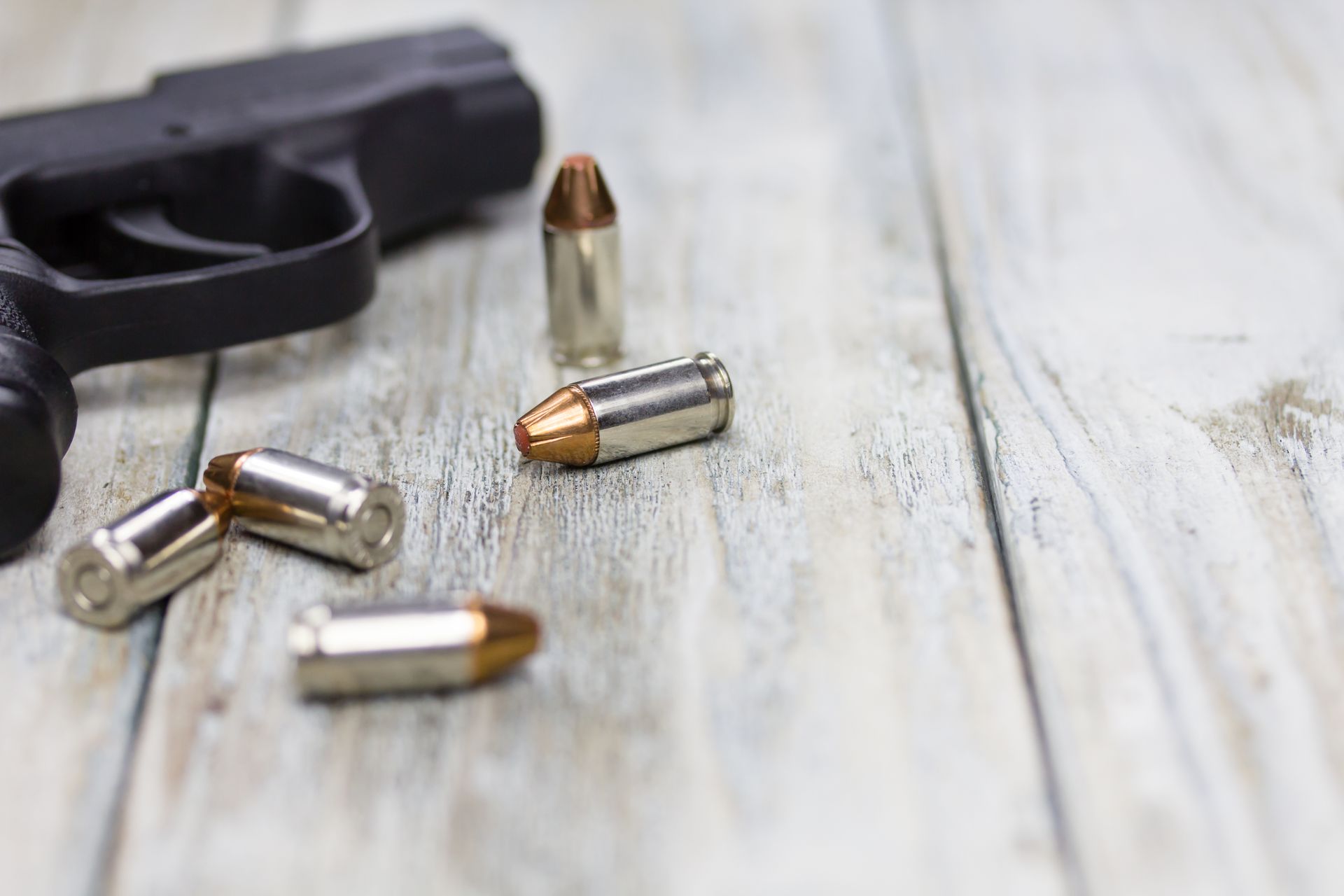 Black handgun with several bullets on a light wooden surface.